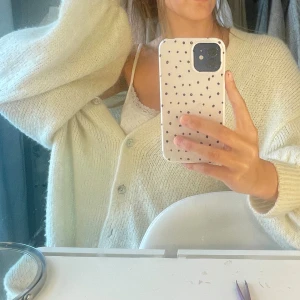 Krämvit stickad kofta med knappar - Supermysig krämvit stickad kofta med v-ringning och stora knappar framtill. Koftan har en loose passform och långa ärmar, perfekt att slänga på sig över ett linne. Enkel och stilren design som passar till allt.