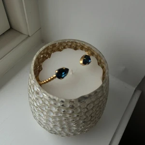 Caroline Svedbom armband  - Snyggt armband i guldfärg med tvinnad design och två stora blå glittrande stenar i varje ände från Caroline svedbom. Perfekt statement-piece som drar blickarna till sig och ger en lyxig känsla till din outfit.