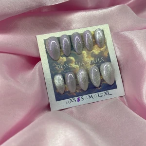 LavendelAura(S);Short Almond;Curved - Säljer ett set med handgjorda press-on naglar i storlek S: 15 mm, 11,5 mm, 12 mm, 11 mm, 9 mm. Naglarna har en snygg ljus lila bas med skimrande cateye glittereffekt och en elegant, mandelformad design. Perfekt för dig som vill ha en trendig och glam look utan att gå till salong.