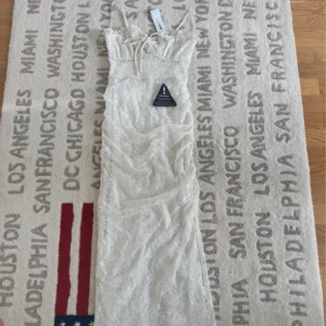 Broderad långklänning från Gina Tricot - Superfin långklänning från Gina Tricot i ljus beige med broderade blommor. Klänningen har smala axelband, söt snörning framtill och en slits bak. Materialet är polyester och ger en lyxig känsla. Perfekt för dig som vill ha en romantisk och trendig look.