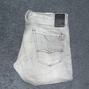 Replay Waitom jeans - Snygga ljusgrå Replay Waitom jeans med klassisk femficksdesign och raka ben. Jeansen har svarta detaljer på bakfickorna och ett svart Replay-märke i midjan. Midja 46cm, längd 103cm. JAG SKICKAR EJ FLER BILDER NÄR JAG BÄR JEANSEN! för storleksguide hänvisar jag till måtten och för bättre inblick i passformen rekommenderar jag att googla på modellnamnet. Jeansen kan vara uppsydda utan att jag noterat det så kolla måtten noggrant :) 40