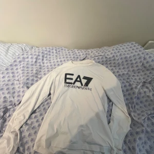Vit långärmad tröja EA7 Armani - Snygg vit långärmad tröja från EA7 Emporio Armani med stor svart logga framtill. Tröjan har rund halsringning och är tillverkad i mjuk bomull, perfekt för en clean och stilren look. Säljs eftersom den är för stor för mig, använt mindre än 5 gånger! Pris i butik 799. Pris diskuteras.