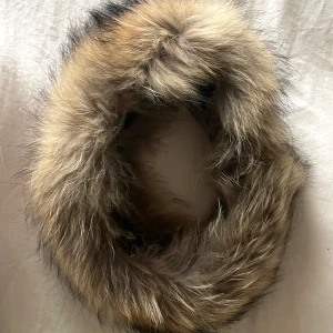 Brun fluffig pälshalsduk - Äkta racoon päls med naturliga bruna och beige toner. Den är ca 70 cm lång och har en riktigt fluffig och varm känsla, perfekt för kalla dagar. Snygg accessoar som ger din outfit/jacka/luva en exklusiv touch.