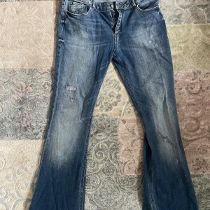 Blå bootcut jeans från Charro - Säljer ett par blå bootcut jeans från Charro med snygga slitningar och broderad detalj på myntfickan. Baktill finns broderade mönster på fickorna. Jeansen har klassisk femficksdesign och normal passform. Perfekt för dig som gillar retrovibe och coola detaljer. Lite defekter på slutet av bena (kolla sista bilderna)  midjemått 38cm 