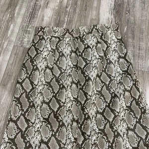 Kort kjol med ormmönster från H&M Divided - Säljer en kort kjol från H&M Divided i storlek 32 med grått och vitt ormmönster. Kjolen har en snygg dragkedja framtill med två silvriga knappar i midjan. Materialet är polyester med en mjuk insida. Perfekt för dig som gillar djurprint och vill sticka ut.