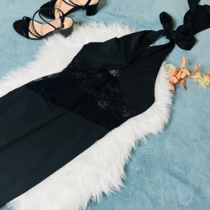 Svart långklänning med spetsdetalj - Svart långklänning med snygg omlott-hals och knyt i nacken. Klänningen har en transparent spetsdetalj över midjan som ger en cool kontrast. Modellen är ärmlös och har en elegant, figurnära passform som framhäver siluetten.