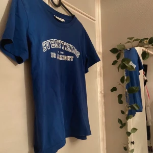 Blå t-shirt från Kappahl med tryck - Blå t-shirt från Kappahl med vit text på bröstet. Klassisk rund halsringning och korta ärmar. Skön passform och tillverkad i mjuk bomull, perfekt till jeans, mjukisbyxor eller annat.