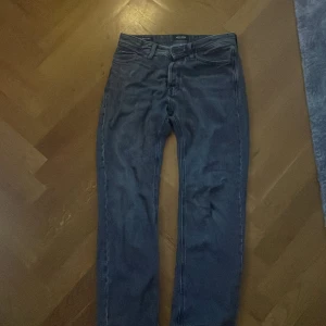 Jack & Jones svarta relaxed jeans - Svarta jeans från Jack & Jones med relaxed fit och klassisk femficksdesign. Jeansen har en mörk tvättad look, raka ben och normal midja. Materialet är robust denim med snygga sömmar och detaljer vid fickorna. Perfekt för dig som gillar avslappnad stil.