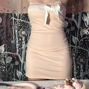 Ljusrosa kort klänning med rosett - Supersöt ljusrosa kort klänning med vit kant upptill och en stor vit rosett framtill. Klänningen är tight och ärmlös, perfekt för dig som gillar en feminin och trendig look. Materialet känns mjukt och stretchigt, vilket gör den bekväm att bära hela dagen.