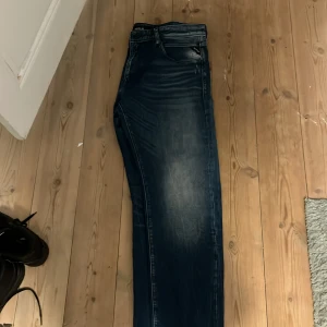 Replay blå jeans, modell Big L - Snygga blå jeans från Replay, modell Big L, med coola slitningar och kontrastsömmar. Klassisk femficksdesign och broderade detaljer på bakfickorna. Jeansen har en rak passform och är tillverkade i slitstarkt denimtyg. Perfekt för dig som gillar streetwear.