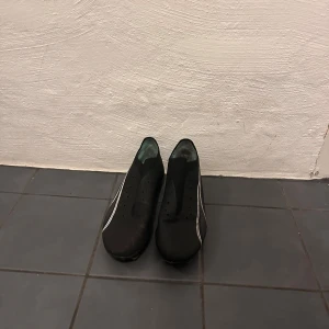 Svarta Puma fotbollsskor med turkos sula - Säljer ett par svarta fotbollsskor från Puma med klassisk vit logga på sidan och turkos innersula samt dobbar. Skorna har låg profil, perforerade detaljer för ventilation och är tillverkade i syntetmaterial för lätt känsla på planen.