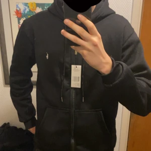 Svart hoodie från Polo Ralph Lauren - Svart hoodie från Polo Ralph Lauren med klassisk vit logga på bröstet. Medium storlek, säljer denna för att jag redan har en exakt samma…