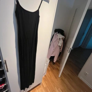 Svart långklänning från Nelly - En stilren svart långklänning från Nelly med smala axelband och rak passform. Klänningen är enkel och tidlös, perfekt för dig som gillar minimalistisk stil. Materialet är mjukt och följsamt, vilket gör den bekväm att bära hela dagen.