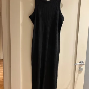 Svart ribbad långklänning Kappahl - Svart ribbad långklänning från Kappahl i storlek S. Ärmlös modell med rund halsringning och figurnära passform. Klänningen är i mjuk stretchig bomull och har en stilren, minimalistisk look som är lätt att styla.