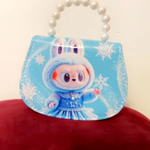 Blå handväska med pärlhandtag - Söt blå handväska med motiv av en tecknad figur i vinterkläder och snöflingor. Väskan har ett pärlhandtag och en avtagbar axelrem i matchande blått. Materialet är syntet och designen är lekfull med vintertema.