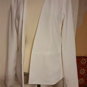 Vit kavaj från Pieces XL - Stilren vit kavaj från Pieces i storlek XL. Modellen är öppen framtill utan knappar och har lång ärm. Materialet är mjukt och har en lätt struktur, vilket ger en snygg och modern look. Perfekt för dig som gillar minimalistisk stil.