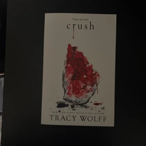 Crush - En spännande bok med mystisk och dramatisk känsla, perfekt för dig som gillar mörka hemligheter och oväntade vändningar. Omslaget pryds av en blodröd kristall och texten 'Trust no one', vilket lockar till läsning för unga vuxna som söker något intensivt och fängslande.