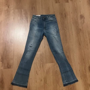 Blå jeans från Dondup 25 - Bootcut jeans från Dondup Ollie i en snygg ljusblå tvätt med slitningar och skinny passform. Klassisk femficksmodell med dragkedja och knapp, samt råa kanter vid benslut. Perfekt för dig som gillar en cool och avslappnad stil. Midja 28cm längd 90cm (74)