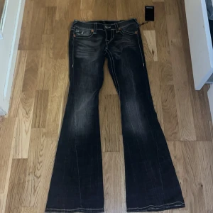 True Religion Joey Low Rise Flare Jeans - Säljer ett par mörkgrå True Religion Joey jeans med låg midja och flare-ben. De har tydliga kontrastsömmar, klassiska fem fickor och snygga detaljer på bakfickorna. Materialet är jeans med slitningar. Jeansen är uppvikta på sista bilden, pris kan diskuteras