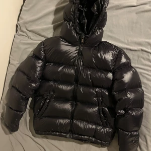 Svart Mayajacka från Zara - Säljer en svart, glansig pufferjacka från Zara med huva och dragkedja framtill. Jackan liknar Moncler Maya och Ralph Lauren The Gorham Glossed Down Jacket. Jackan är vadderad och har en riktigt fet, oversized look som passar perfekt när det är kallt. Jackan är även Väldigt eftertraktad. Riktigt snygg och trendig vinterjacka. Mitt pris 529. För mer bilder/frågor skriv dm