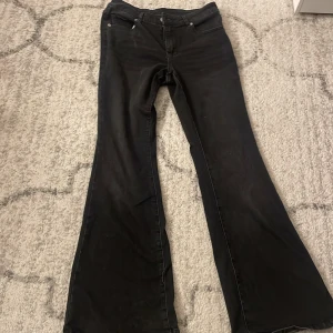 Svarta bootcut jeans - Säljer ett par svarta jeans med bootcut passform och klassisk femficksdesign. Byxorna har en snygg utsvängd siluett från knäet och är tillverkade i mjukt jeanstyg. Perfekta för dig som gillar retrovibbar och vill sticka ut med en cool look.