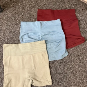 3-pack sömlösa shorts i pastellfärger - Säljer tre par sömlösa shorts med hög midja i färgerna ljusbeige, ljusblå och vinröd. Perfekta för träning eller chill, med stretchigt material och ribbad midja för extra komfort.