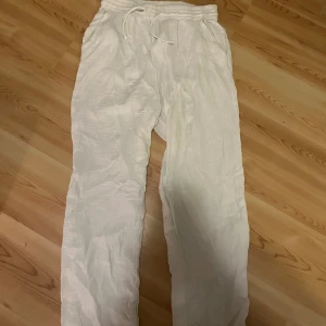 Vita linnebyxor från Gina Tricot - Säljer ett par vita linnebyxor från Gina Tricot i storlek 36. Byxorna har rak passform, resår i midjan och snörning för extra komfort. Perfekta för chill dagar och har en lätt, luftig känsla tack vare linnematerialet.