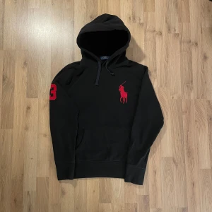 Svart hoodie från Polo Ralph Lauren - Svart hoodie från Polo Ralph Lauren med stor röd logga på bröstet och röd siffra 3 på ärmen. Tröjan har huva med snörning och en klassisk känguruficka framtill. Mjuk bomullskvalitet och långärmad modell, perfekt för chill dagar.  Bilder på måtten finns tillgängliga. Fråga gärna! Snabb leverans!