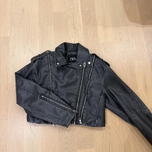 Svart skinnjacka från Zara - Snygg svart skinnjacka från Zara med croppad passform och coola detaljer som dragkedjor och axelklaffar.  Helt oanvänd. 