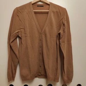 Beige kofta med v-ringning och knappar - Snygg beige kofta från Herrysoft med v-ringad hals och knappar framtill. Långärmad och mjuk stickad känsla, perfekt för lager-på-lager. Enkel design som funkar till många olika stilar.