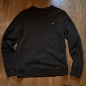 Mörkgrön sweatshirt från Lyle & Scott - Säljer en sweatshirt från Lyle & Scott i mörkgrön färg. Tröjan har använts ett fåtal gånger och är till synes utan och innan i nyskick. Tröjan har den klassiska gula fågeln broderad på vänster bröst med en minimalistisk design. Passar utmärkt för kyligare väder