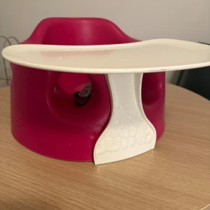 Bumbo Babysitter med Bricka - Praktisk Bumbo babysitter i röd färg med avtagbar vit bricka. Perfekt för små barn som lär sig sitta. Brickan är lätt att rengöra och stolen har säkerhetsbälte. Några mindre märken finns, men överlag i gott skick.