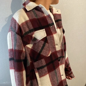 Rutig höst/vår jacka från Zara i rött - Höst/vår jacka från Zara i röd och vit rutig design. Skjortan har klassisk krage, stora bröstfickor med knappar och långa ärmar. Materialet är mjukt och lite tjockare. Stängs med knappar framtill. Ger en väldigt stilig look. Knappt använd.