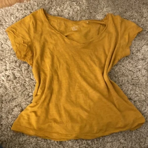 Gul t-shirt med v-ringning från Lindex - Säljer en enkel gul t-shirt från Lindex i storlek XS. Toppen har v-ringad hals och korta ärmar, tillverkad i mjuk bomull. 