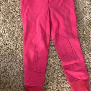 Rosa ridbyxor från CRW med hjärtdetalj - Snygga rosa ridbyxor från CRW i mjukt bomullsmaterial. Byxorna har förstärkningar på insidan av benen, två bakfickor med text och glittrigt hjärta, samt bekväm midja.