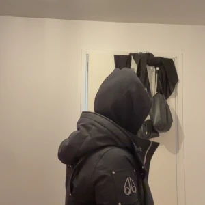 Svart pufferjacka från Moose Knuckles - Säljer en svart pufferjacka från Moose Knuckles med stor huva och snygga detaljer på ärmen. Jackan har dragkedja och knappar framtill, quiltad design och en riktigt schysst passform som håller dig varm. Perfekt för dig som gillar streetstyle och vill ha något som sticker ut. Jag har använt den i två vinter det därför den kostar så litet oxå kör av dig för mer information 