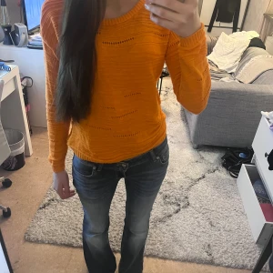 Orange stickad tröja med hålmönster - Säljer en snygg orange stickad tröja med hålmönster och rund hals. Tröjan har långärmade ärmar och en lätt loose passform. Perfekt för dig som gillar färg och vill ha något som sticker ut lite extra i garderoben.