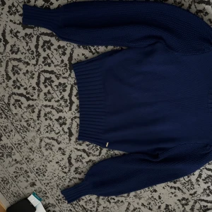 Marinblå stickad tröja med puffärm - Snygg marinblå stickad tröja med bred ribbad mudd i midjan och vid ärmslut. Tröjan har puffiga långärmar med grovstickad struktur som ger en cool och trendig look. Perfekt att matcha med jeans eller kjol för en chill stil.