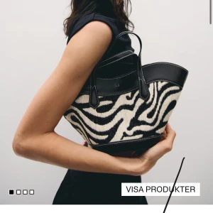 Zebramönstrad handväska i skinn - Cool handväska med zebramönster i svart och vitt, detaljer i svart skinn och kontrastsömmar. Väskan har två handtag och en rymlig form som gör den perfekt för att bära med sig allt man behöver. Perfekt statement piece för din outfit.