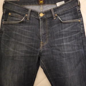 Mörkblå jeansshorts från Lee W29 L32 - Snygga mörkblå jeansshorts från Lee med klassisk femficksdesign och guldfärgade detaljer. Shorts i rak modell med normal passform och slitna tvättade partier för en cool look. Perfekta för dig som gillar streetstyle och denim. Mycket fint skick 