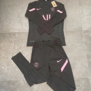 PSG x Nike svart träningströja S - Svart långärmad träningströja från Nike x PSG med halv dragkedja, rosa detaljer och diskret mönster. Tröjan har PSG-logga på bröstet, Dri-FIT ADV-tyg och rosa Nike-logga. Perfekt för fotbollsträning eller chill dagar.