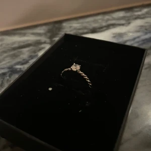 Silverring med glittrande sten - Snygg och stilren silverring med en glittrande rund sten i mitten. Ringen har en tvinnad design som ger den en unik och modern look. Perfekt för dig som gillar enkla men ändå iögonfallande smycken. Passar både som statement eller att kombinera med andra ringar.