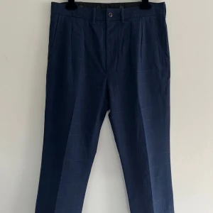 Mörkblå rutiga kostymbyxor RRL - Snygga mörkblå kostymbyxor från RRL Ralph Lauren med diskret rutmönster. Byxorna har klassisk rak passform, bälteshällor och fickor fram och bak. Materialet är en lyxig mix av bomull, ull och linne som ger en skön känsla och stilren look. Nypris 5000 kronor. Nyskick, storlek W32,L32