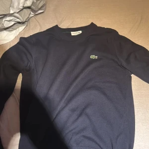 Lacoste stickad tröja - Snygg mörkblå stickad tröja från lacoste som max använts 3 gånger, alltså är den iprincip ny. Regular fit och perfekt för dig som gillar stilrena plagg med diskret branding.
