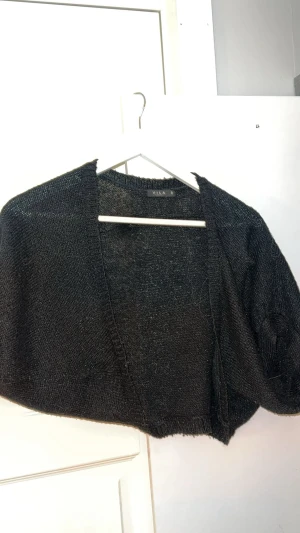 Svart stickad kofta från Vila - Säljer en svart lite glittrig fin Bolero från Vila i storlek S. Koftan har en enkel design utan knappar eller dragkedja och är gjord i ett tunt stickat material som passar perfekt för lager-på-lager och speciellt nu inför Nyår 😚Snygg att slänga över en topp ex. I fint skick och Skicka vid fler frågor eller Annars Är de bara att köpa 🥰