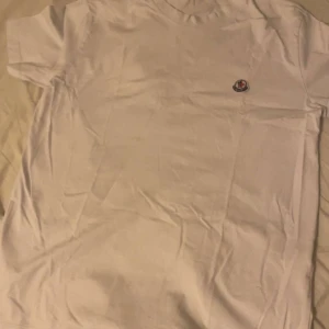 Vit Moncler t-shirt  - Snygg vit t-shirt som är moncler. Klassisk passform med korta ärmar och rund hals. Diskret Moncler-logga broderad på bröstet. Perfekt för dig som gillar stilrena och exklusiva plagg.