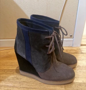 Kilklack mocka Reschia Flerfärgad 37 12.5 cm Nyskick - Snygga boots med kilklack i brun och mörkblå mocka. Skorna har snörning framtill och en rund tå. Perfekta för dig som vill ha höjd men ändå stabilitet. Materialet är mjuk mocka och färgerna är diskret kombinerade för en cool look.