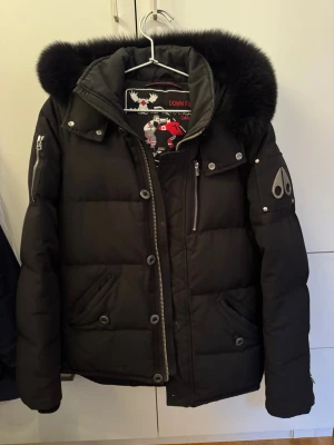 Svart dunjacka Moose Knuckles - Svart dunjacka från Moose Knuckles med stor fluffig päls på huvan. Jackan har flera dragkedjor, knappar och snygga detaljer på ärmen. Insidan har broderad hockeygrafik och logga. Perfekt för kalla vinterdagar. Storlek S. Använd men fortfarande i bra skick. Nypris låg på runt 7-8000kr om jag minns rätt. Priset är förhandlingsbart.