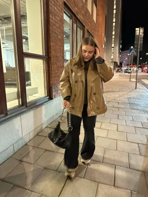 GANNI jacka - Vinyljacka i ljusbrunt från GANNI. Sparsamt använd. Sjukt cool! Köpt för 6800kr. Säljs ej längre.