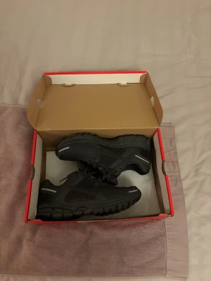 Nike Zoom Vomero 5 Svarta sneakers - Nike Zoom Vomero 5 sneakers i helsvart färg med mesh och syntetdetaljer. Snygg sportig design med rund tå, platt sula och snörning. Märket syns tydligt på plösen och sidan. Perfekta för dig som gillar stilrena och bekväma skor.